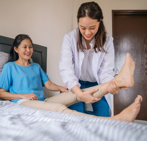 Qualicare nurse providing in-home foot care to a smiling senior client