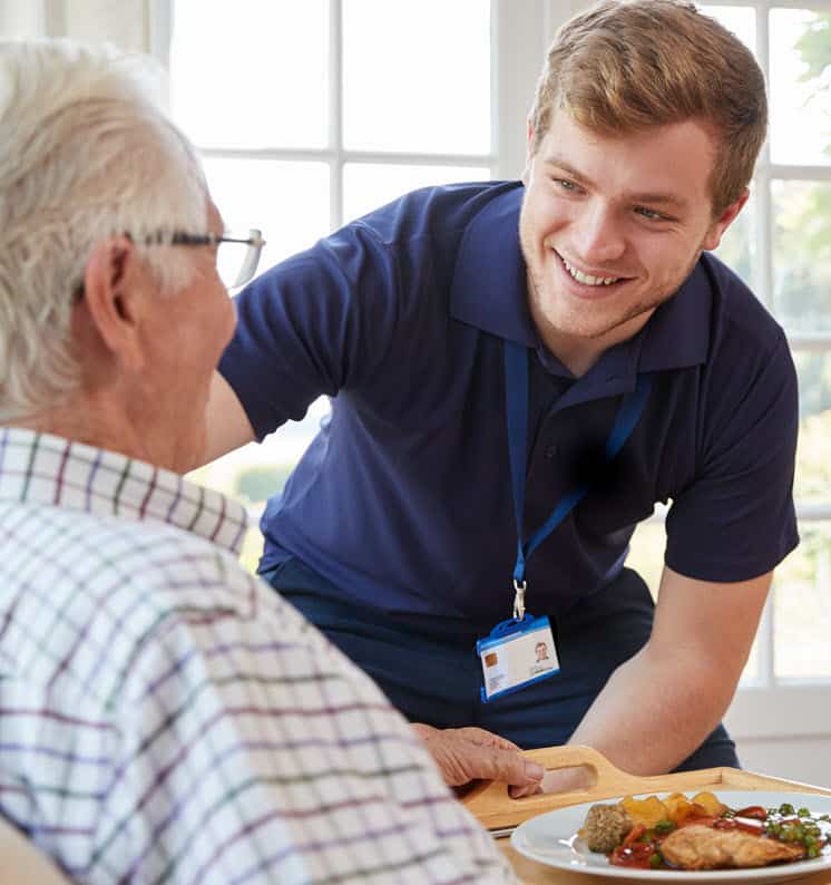 provider of senior care in Oshawa smiling with elderly patient holding food tray